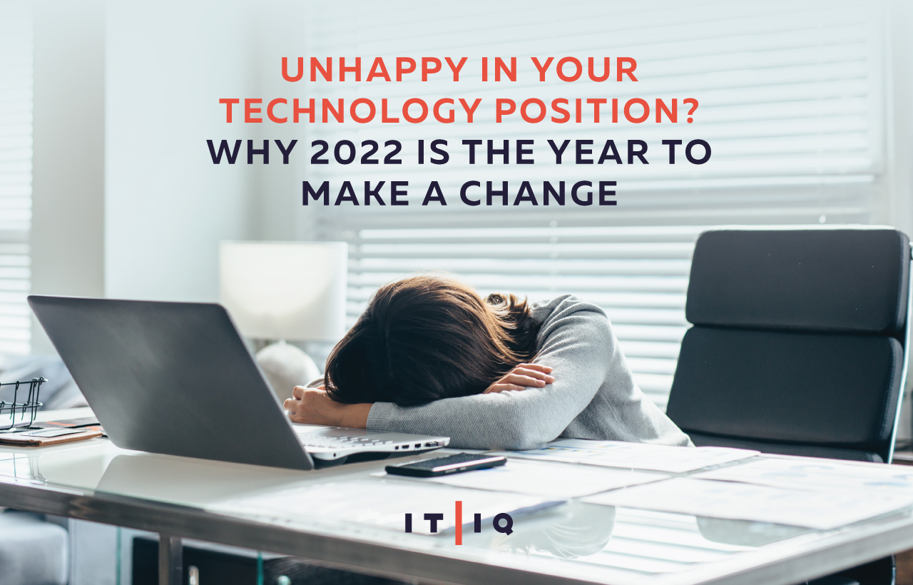 Woman hides her face and slumps over at her desk with text Unhappy in Your Technology Position? Why 2022 Is the Year to Make a Change