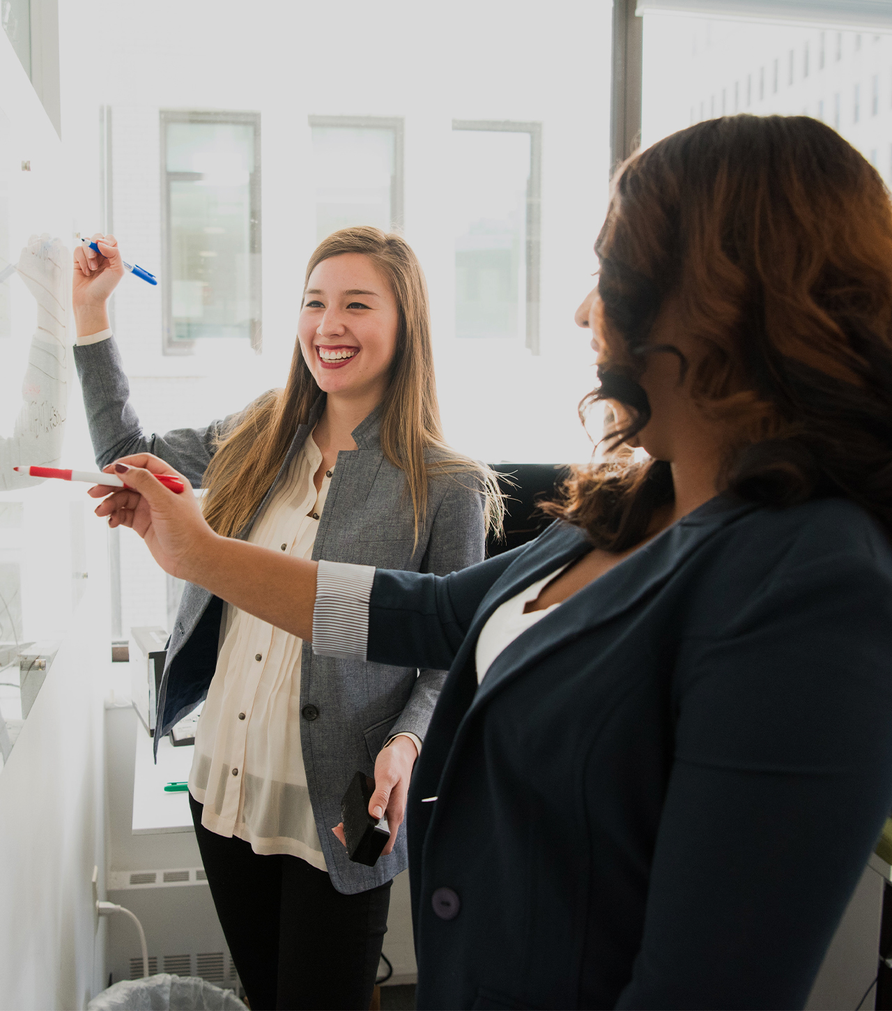 Two business women draw up ideas on a whiteboard